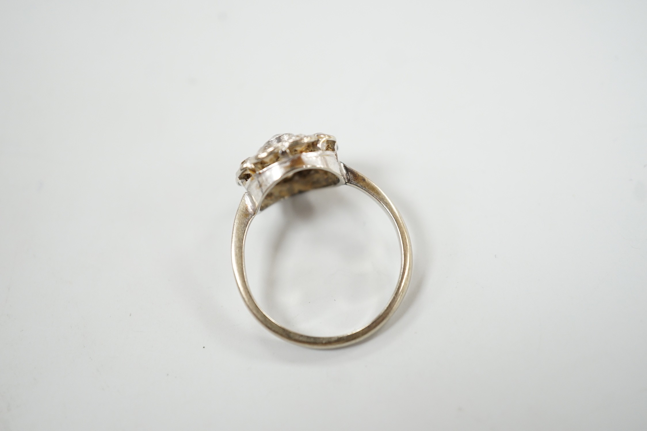 A 1920's white metal and ten stone millegrain set diamond flower head cluster ring, size P/Q, gross weight 3 grams.